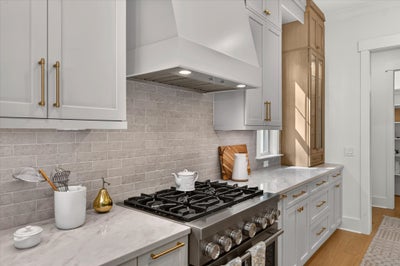Kitchen with gray cabinets, gold hardware, gas range, white range hood, and gray tile backsplash