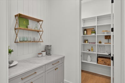 Butler's pantry with marble countertop, gold wall shelves, and walk-in pantry with built-in white shelving