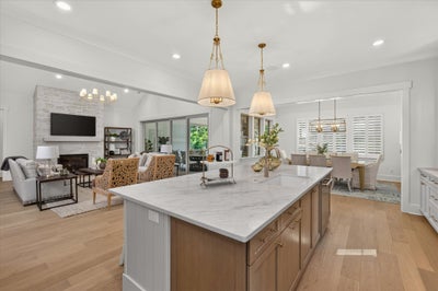 Open-concept kitchen with marble island, pendant lights, and wood floors flowing into living and dining areas with stone fireplace.