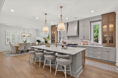Open kitchen with large marble island, gray cabinets, pendant lights, and hardwood floors, open to dining area