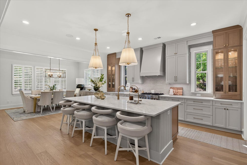 Open kitchen with large marble island, gray cabinets, pendant lights, and hardwood floors, open to dining area