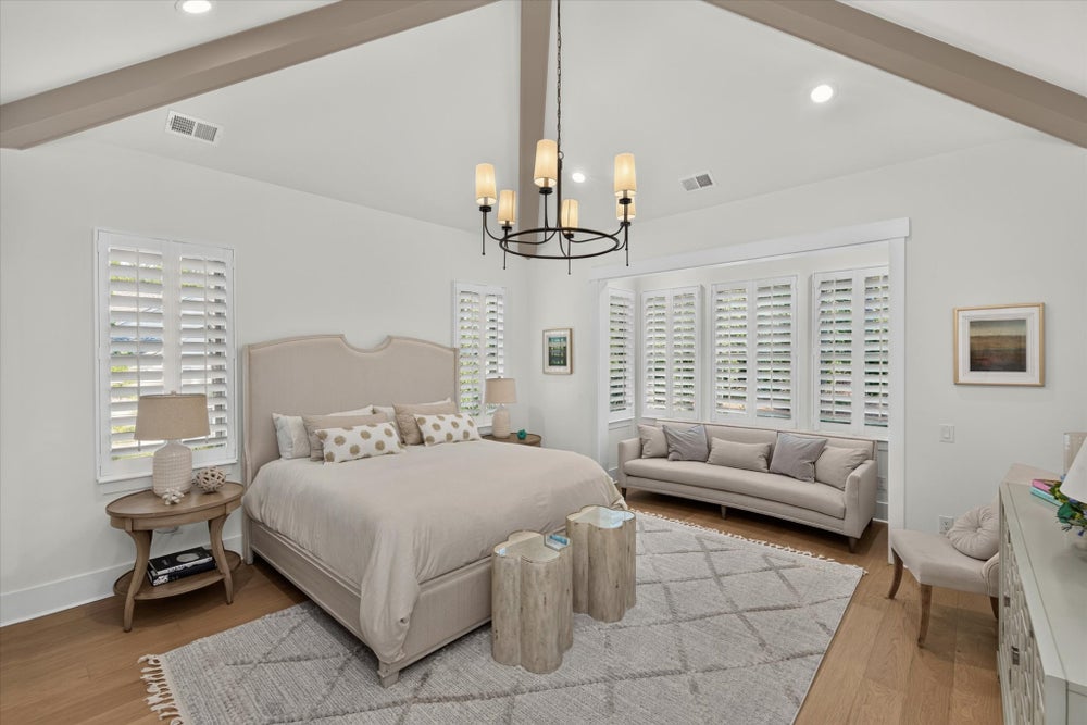 Spacious master bedroom with vaulted beamed ceiling, chandelier, plantation shutters, and hardwood floors