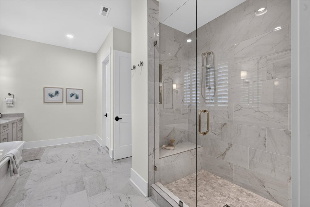Large walk-in shower with glass door, marble tile walls, built-in bench, and matching marble floor throughout the bathroom.