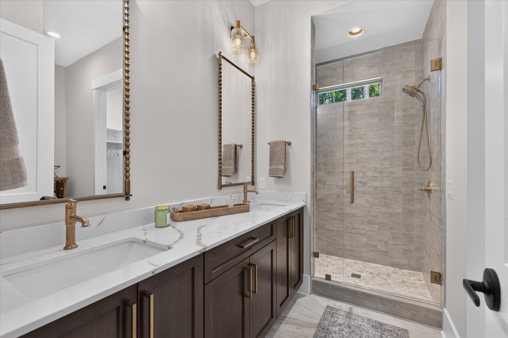 Bathroom with double vanity, dark wood cabinets, marble countertop, gold fixtures, and glass-enclosed tile shower.