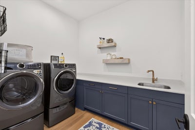 Laundry room with front-load washer and dryer, navy cabinets, white countertop, and utility sink with floating shelves above.