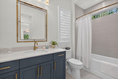 Bathroom with navy vanity, gold fixtures, white quartz countertop, and tub-shower combo with tile surround