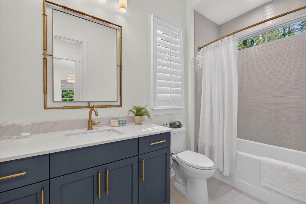 Bathroom with navy vanity, gold fixtures, white quartz countertop, and tub-shower combo with tile surround
