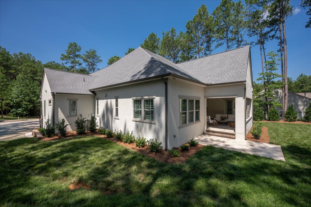 Single-story home with white stucco exterior, gray roof, covered patio, and landscaped yard surrounded by pine trees