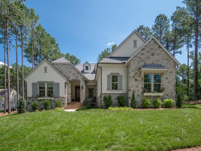 Two-story home with stone and stucco exterior, gray shutters, arched entry, and manicured lawn surrounded by tall pine trees