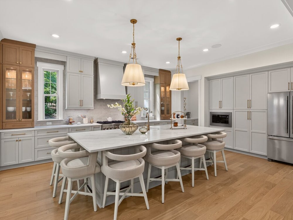 Large kitchen with gray cabinets, marble island with eight stools, pendant lights, and hardwood floors