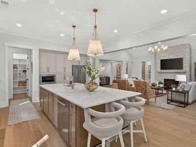 Open-concept kitchen with large marble island, bar stools, and pendant lights, open to living room with stone fireplace