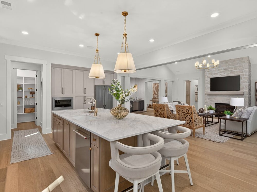 Open-concept kitchen with large marble island, bar stools, and pendant lights, open to living room with stone fireplace