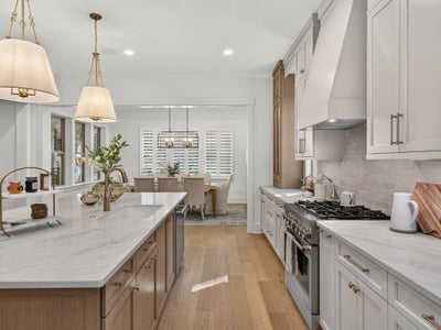 Kitchen with marble island, white cabinets, stainless range, and pendant lights opening to dining area with hardwood floors
