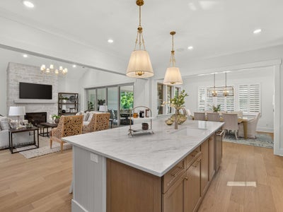 Open-concept kitchen with large marble island, wood cabinets, and pendant lights, flowing into living and dining areas with stone fireplace.