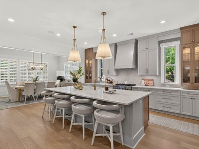 Kitchen with large marble island, gray cabinets, pendant lights, and open dining area with hardwood floors