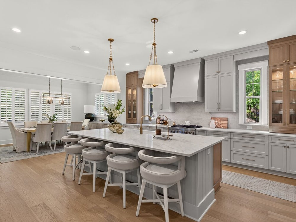 Kitchen with large marble island, gray cabinets, pendant lights, and open dining area with hardwood floors
