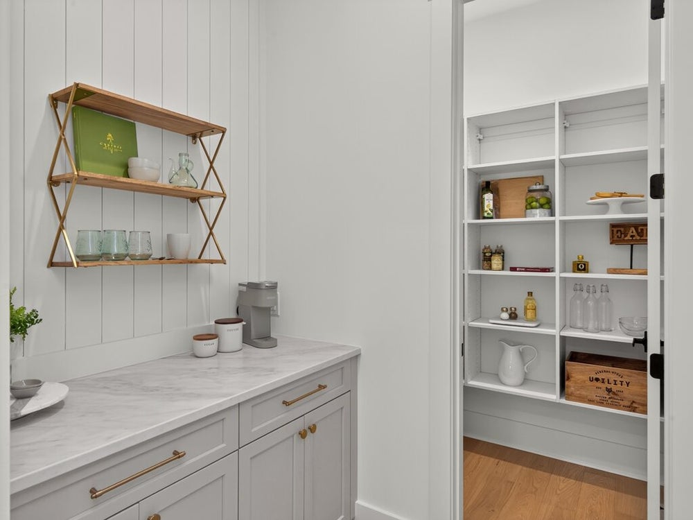 Butler's pantry with marble countertop, gold open shelving, white cabinets, and walk-in pantry with built-in shelves