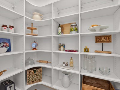 Walk-in pantry with white built-in shelving, curved corners, and adjustable shelves stocked with kitchen items