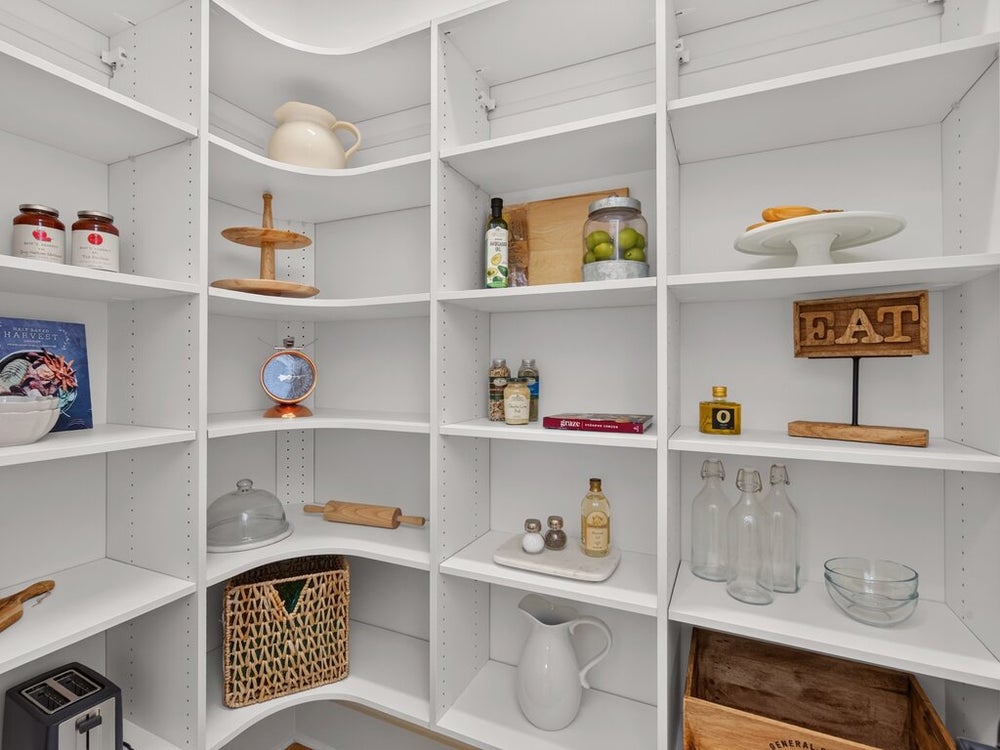 Walk-in pantry with white built-in shelving, curved corners, and adjustable shelves stocked with kitchen items