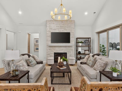Living room with stone fireplace, two neutral sofas, wood coffee table, and gold chandelier overhead