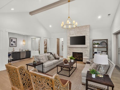 Open living room with vaulted ceiling, stone fireplace, wood beam, and gold chandelier above neutral seating area