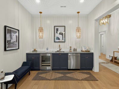 Wet bar with navy cabinets, marble countertop, wine fridge, and two gold pendant lights against shiplap wall