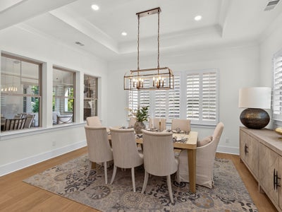 Formal dining room with eight-seat table, bronze chandelier, coffered ceiling, and plantation shutters