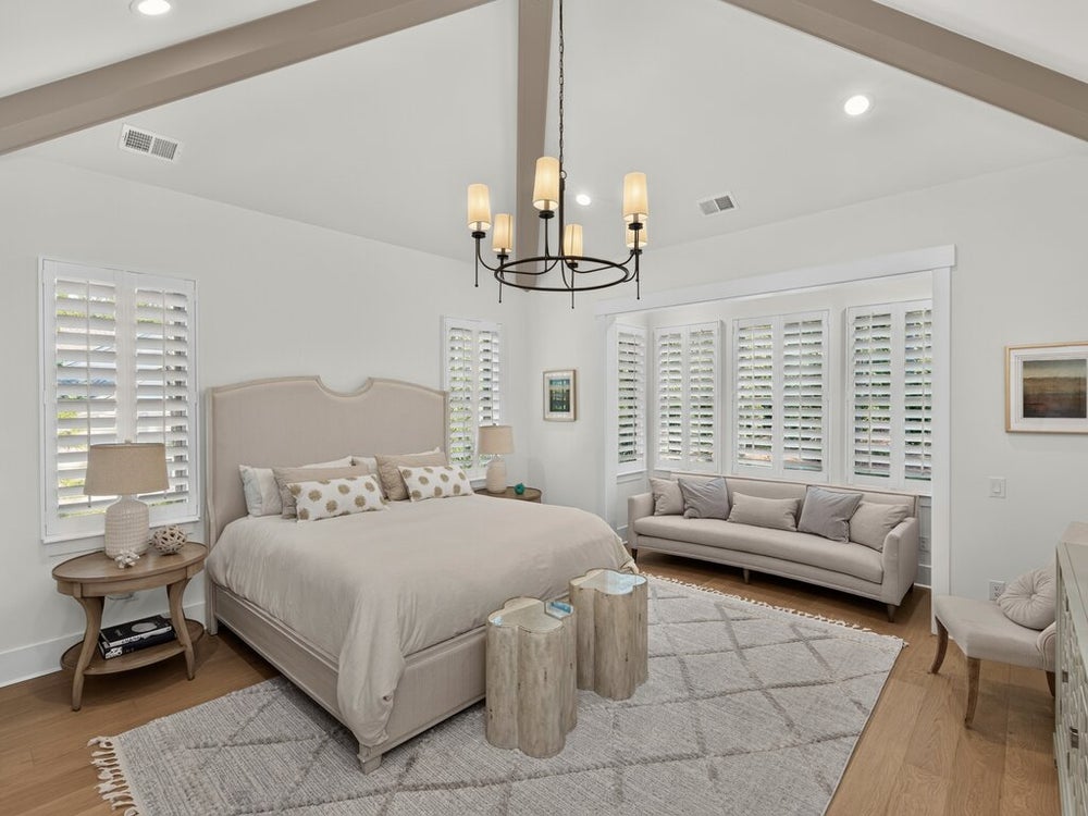 Bedroom with vaulted beamed ceiling, chandelier, plantation shutters, and hardwood floors