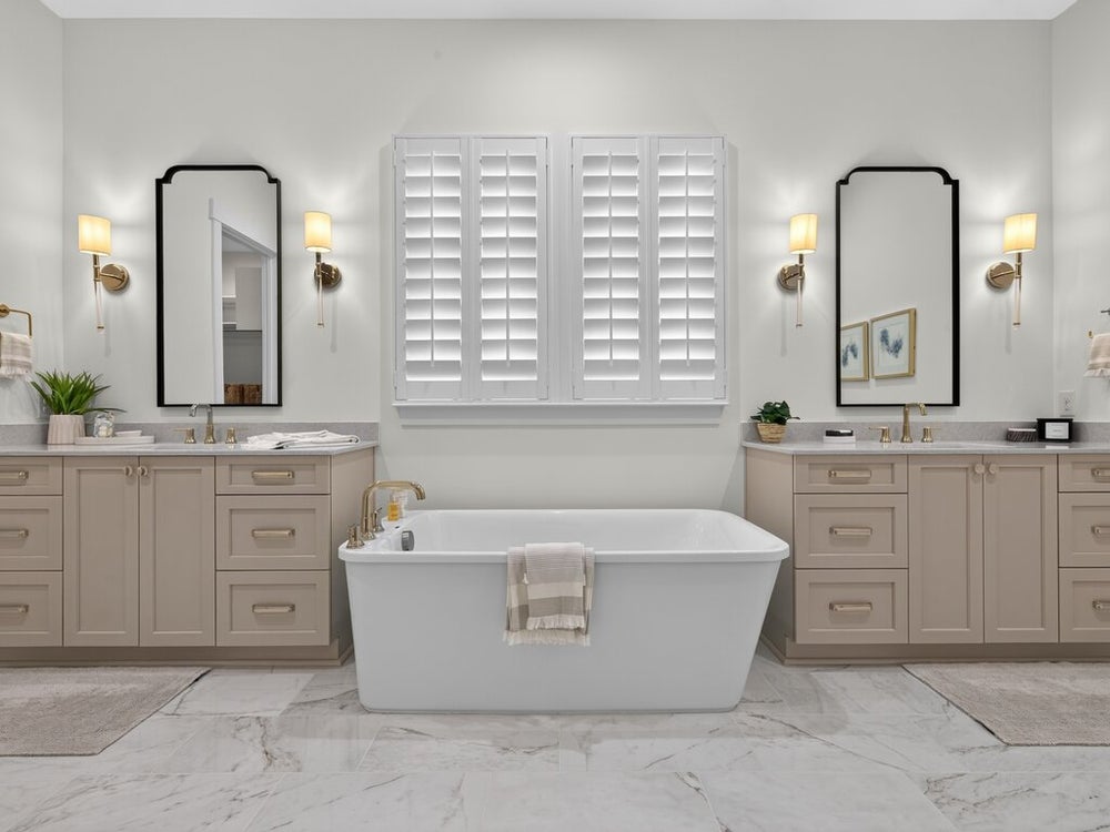 Master bathroom with freestanding soaking tub, dual vanities, marble tile floors, and plantation shutters