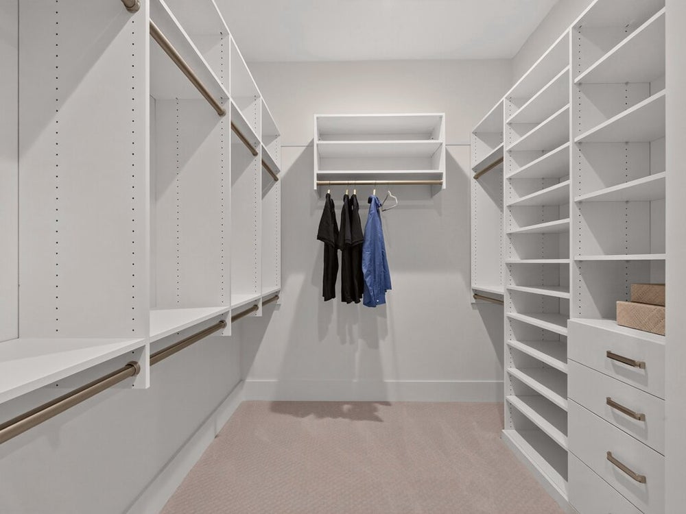 Walk-in closet with white built-in shelving, hanging rods, and built-in drawers on carpeted floor