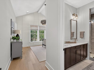 Bathroom vanity with dark wood cabinets and marble countertop beside a hallway with vaulted ceiling and hardwood floors