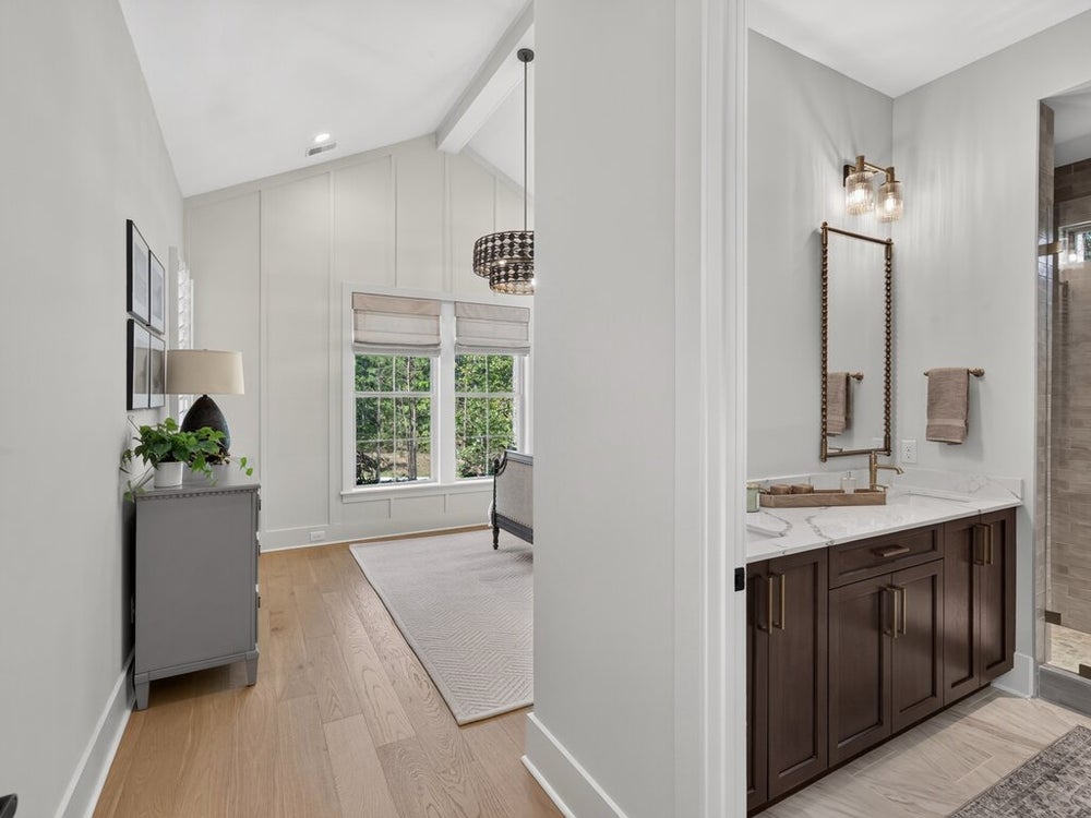 Bathroom vanity with dark wood cabinets and marble countertop beside a hallway with vaulted ceiling and hardwood floors