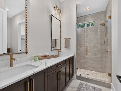 Bathroom with dark wood double vanity, marble countertop, gold fixtures, and glass-enclosed tile shower