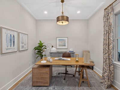 Home office with wood desk, leather chair, pendant light, and crown molding on hardwood floors