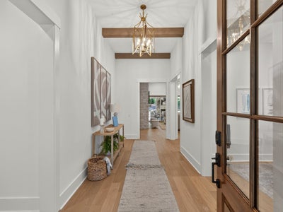 Bright entryway with high ceilings, wood beams, gold chandelier, and hardwood floors leading to main living area