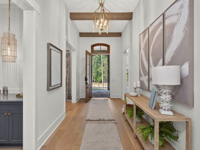 Bright entryway with wood beam ceiling, gold chandelier, hardwood floors, and arched front door