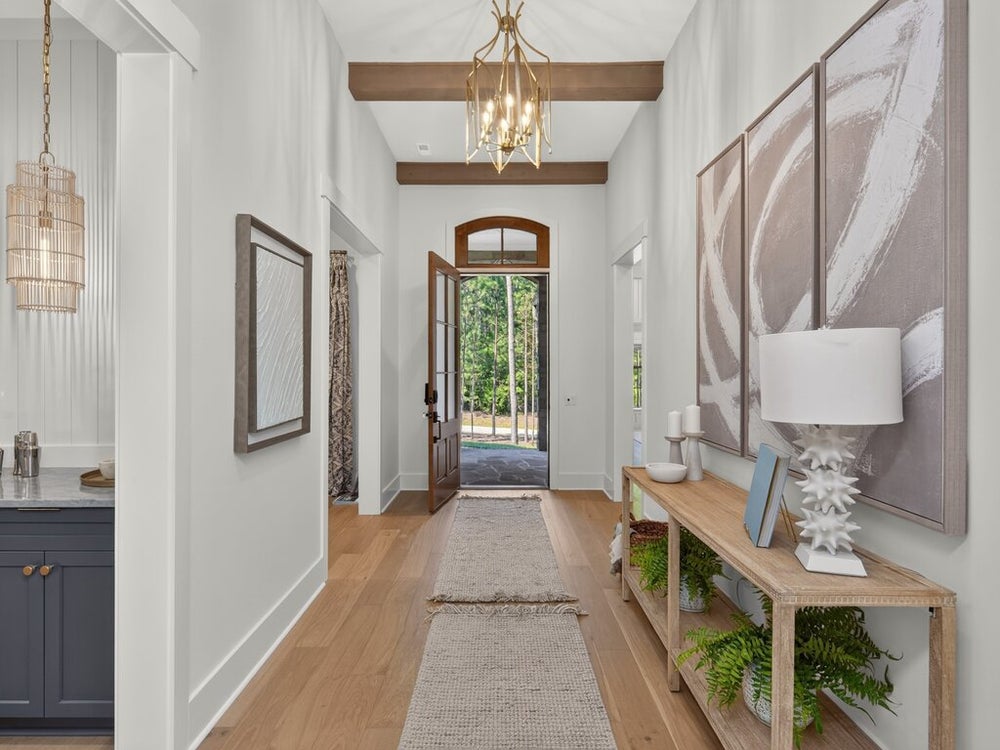 Bright entryway with wood beam ceiling, gold chandelier, hardwood floors, and arched front door