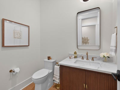 Powder room with wood vanity, marble countertop, gold fixtures, and framed mirror
