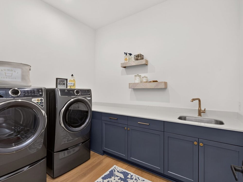 Laundry room with front-load washer and dryer, navy blue cabinets, white countertop, utility sink, and floating shelves