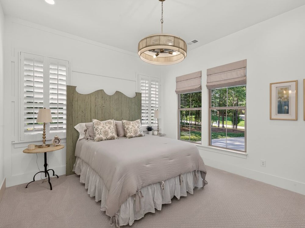 Bedroom with wood headboard, plantation shutters, pendant light, and neutral carpet