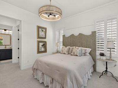 Bedroom with wood headboard, plantation shutters, drum chandelier, and ensuite bathroom visible through doorway
