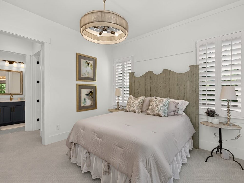 Bedroom with wood headboard, plantation shutters, drum chandelier, and ensuite bathroom visible through doorway