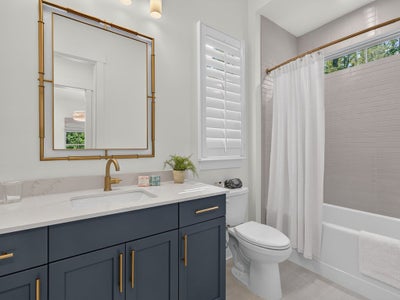 Bathroom with navy vanity, gold fixtures, white countertop, and tub-shower combo with curtain