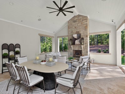 Covered outdoor patio with stone fireplace, dining table, seating area, vaulted ceiling, and ceiling fan