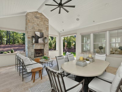 Covered outdoor patio with stone fireplace, dining table, seating area, and vaulted ceiling with ceiling fan.