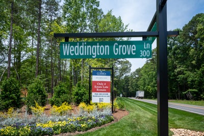 Weddington Grove Lane street sign at subdivision entrance with Classica Homes sales sign and landscaped flower beds nearby.