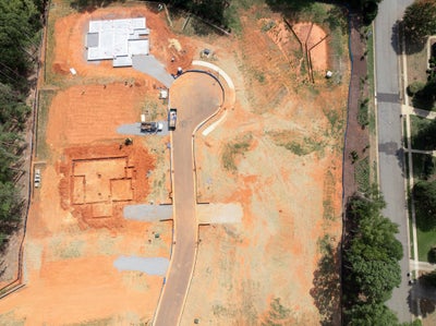 Aerial view of a home construction site with foundation work, paved driveway, and cleared red clay lot