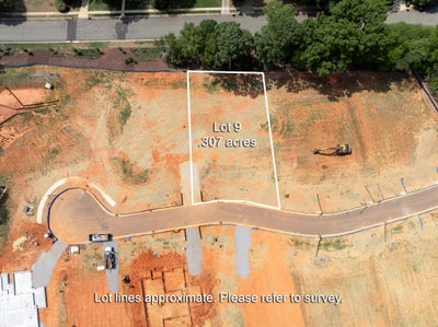 Aerial view of Lot 9, a 0.307-acre vacant residential lot with cleared red clay soil and a curved street frontage.