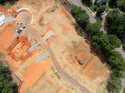 Aerial view of residential construction site with graded red clay lots, paved road, and excavated foundation footings