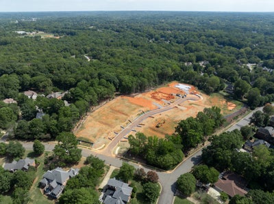 Aerial view of a new residential subdivision under construction with cleared lots and roads surrounded by trees and existing homes.